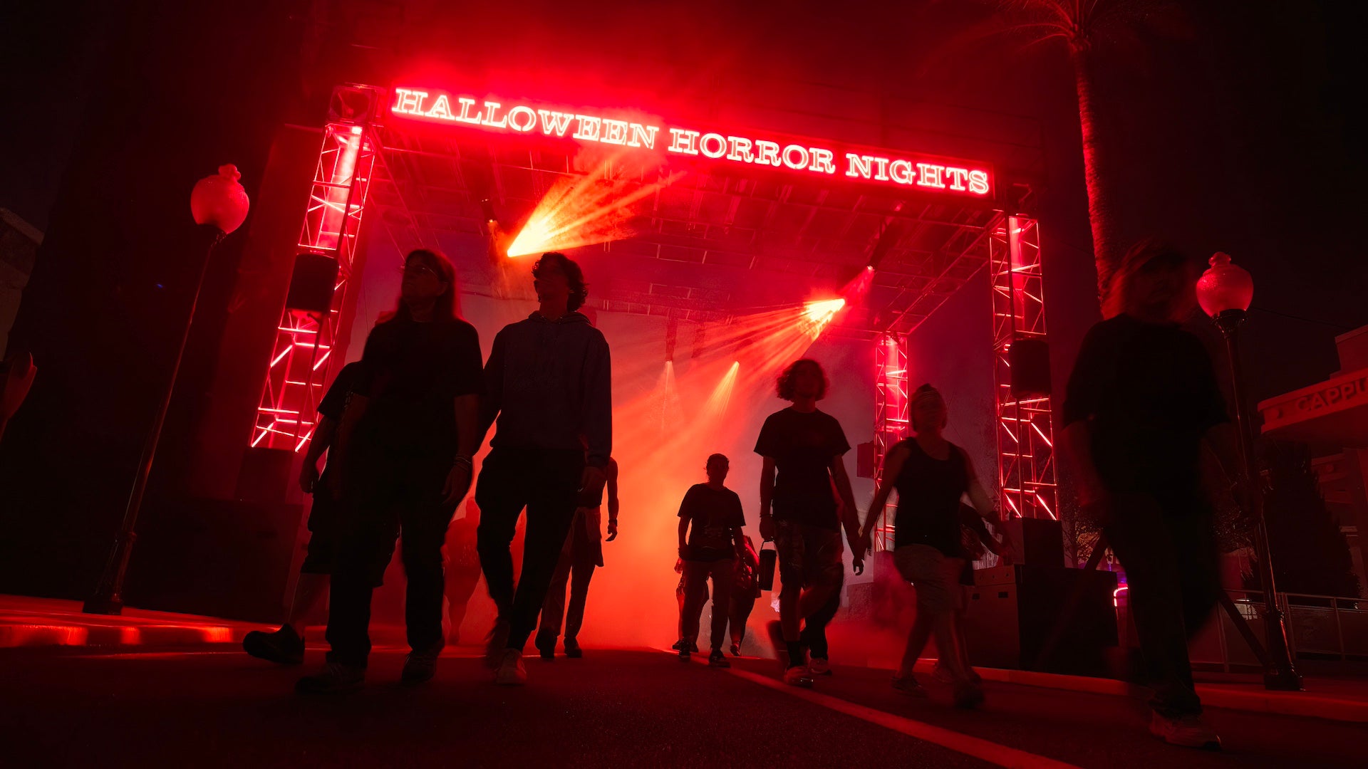 Several people walking under a neon lit sign at the entrance to Halloween Horror Nights in Orlando
